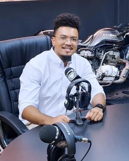 João Victor, de camisa branca, sentado em um estúdio de podcast
